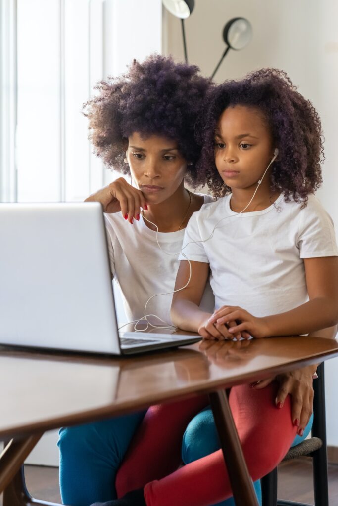 Woman with a girl on her lap wearing headphones and watching something on a laptop.