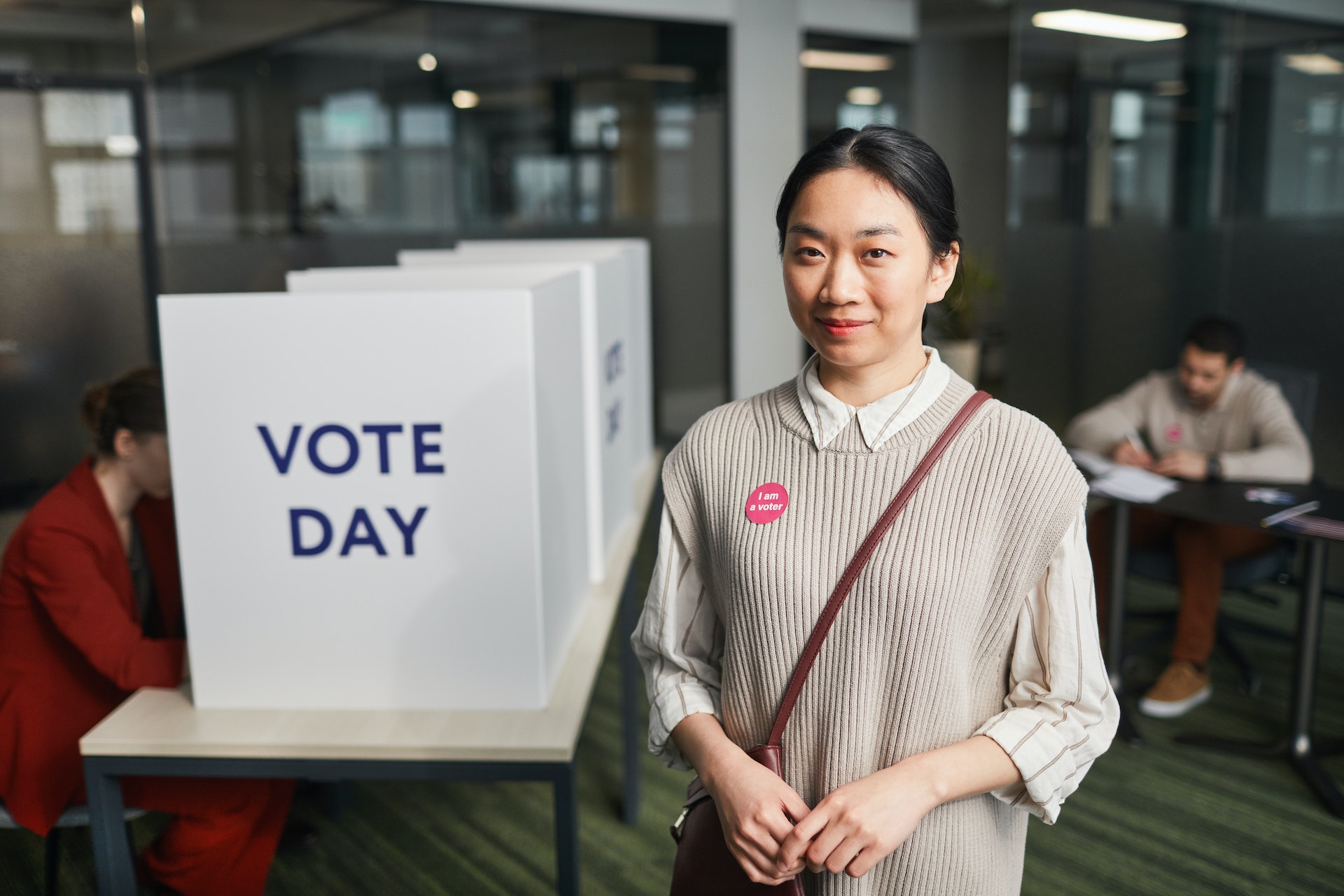 Woman stands in front of a voting booth wearing an "I am a voter" sticker.