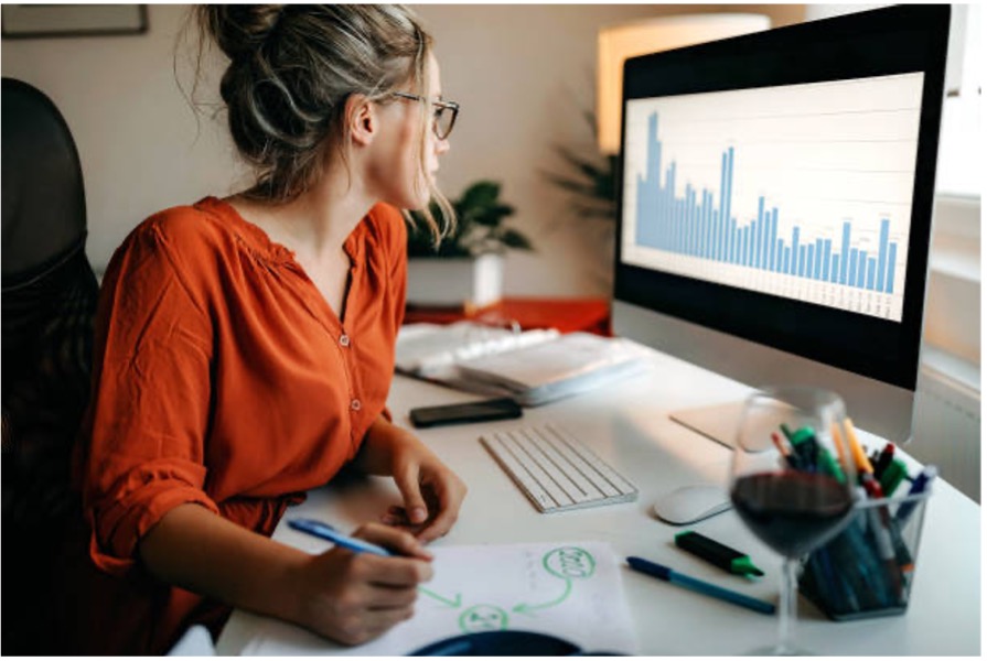A woman at her desk looking at graphs of data and taking notes.