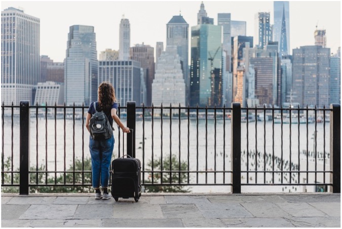 A woman with luggage looking at the New York skyline.