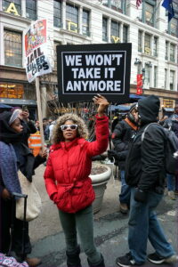 A Black woman holds a sign "We don't take it anymore" during a protest.