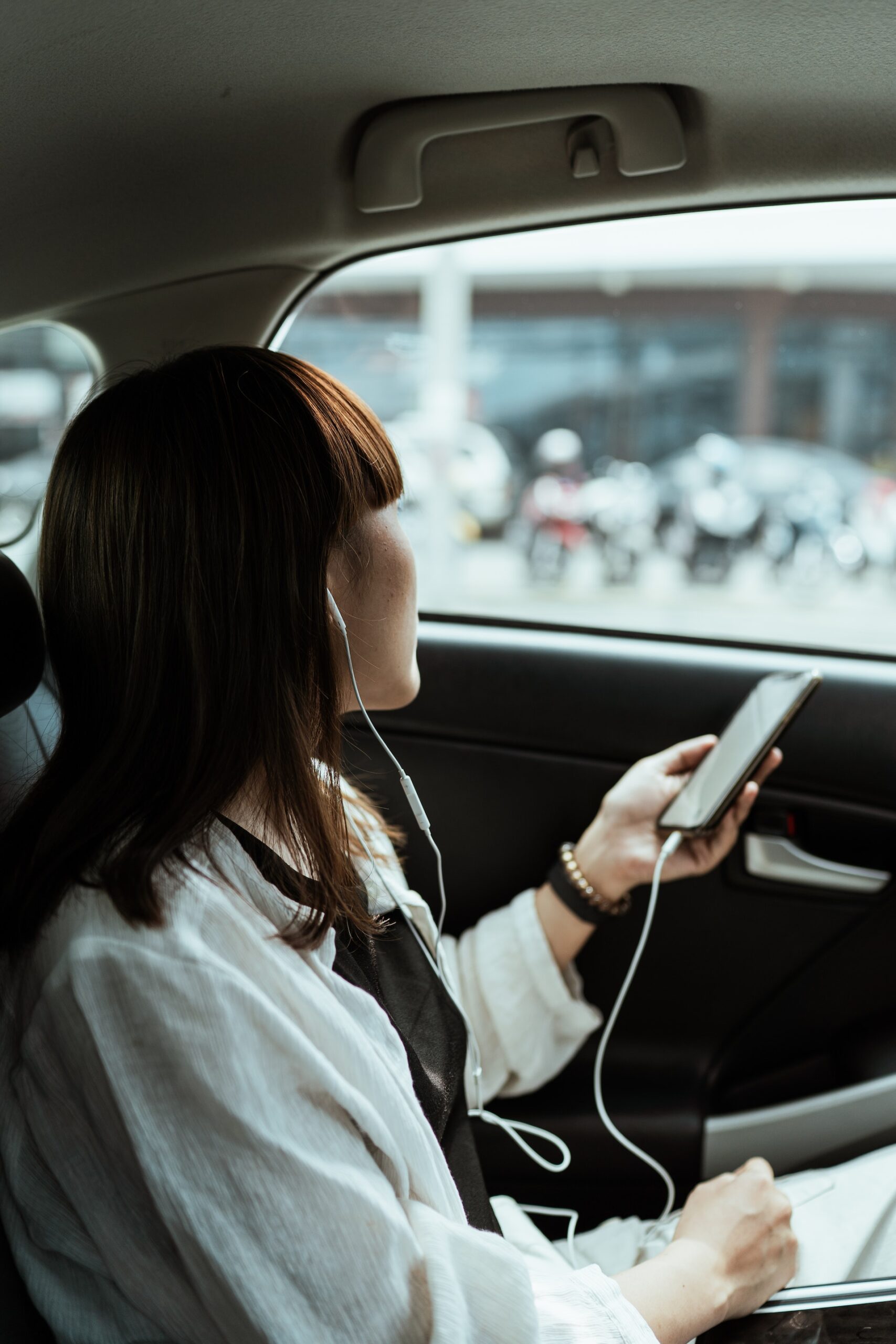 Woman sitting in the backseat of a car listening to music with headphone in.