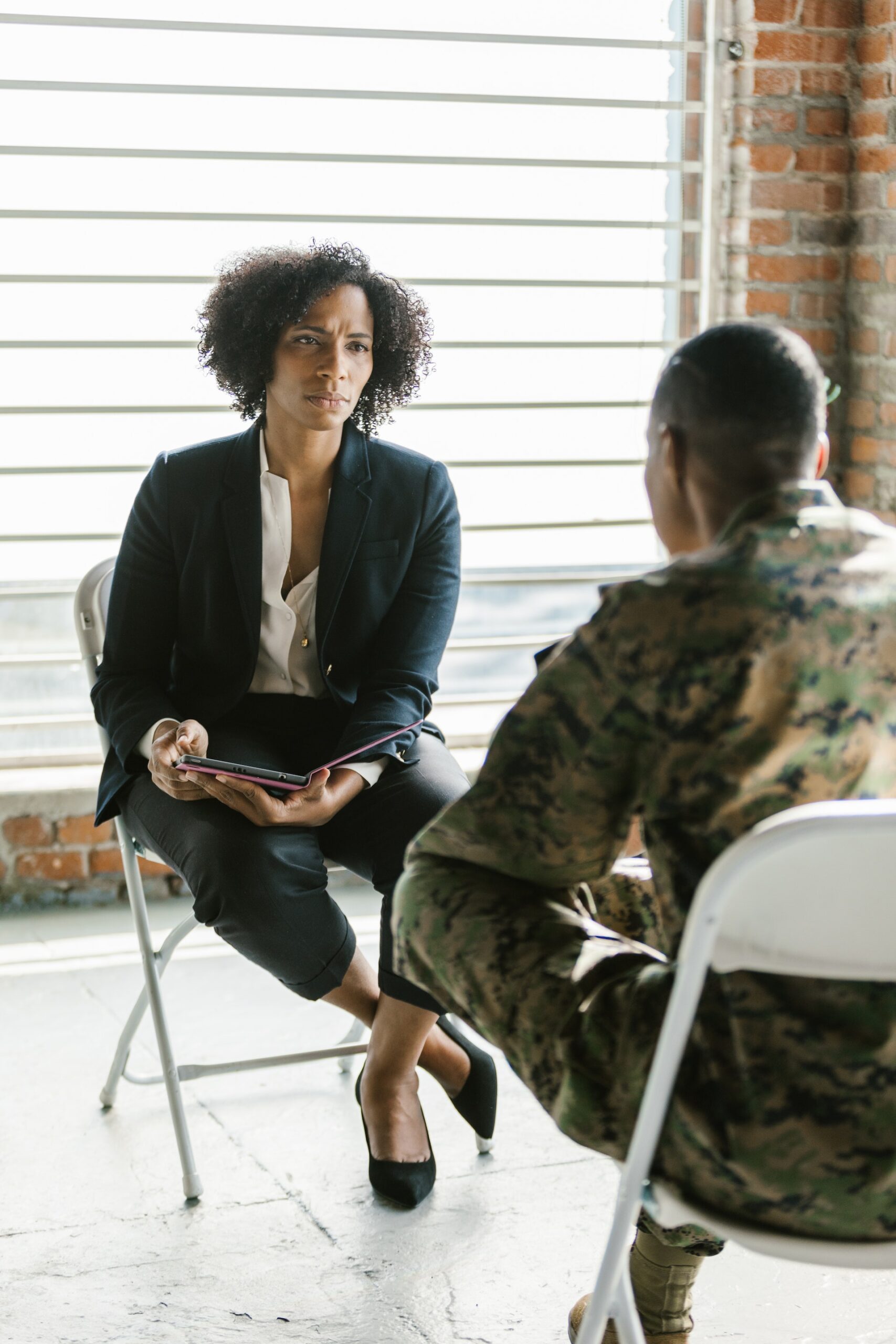 A Black female psychologist listening to a male soldier as they are seated across from eachother.