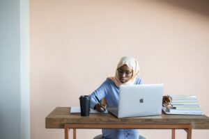 woman sitting at a desk and laptop, writing in a notebook