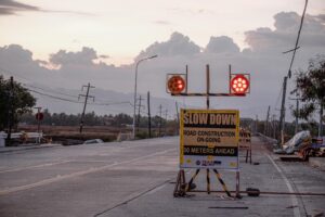 sign with lights warning, "slow down road construction on going 50 meters ahead" on a paved road