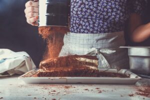 baker messily dusting cake with cocoa powder