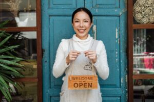 woman standing in front of a business holding a sign that says welcome we are open