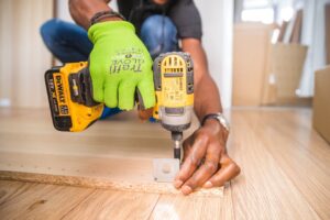 person attaching a metal part to a wooden board with an electric hand held drill