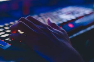 a person's hand typing on a backlit keyboard in a dark room