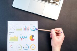 person's hand holding a pen pointing at a document with many charts and graphs