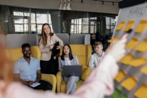 4 people in a business meeting looking at a presenter's whiteboard covered with sticky notes