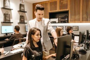manager stands over worker at a computer to direct work