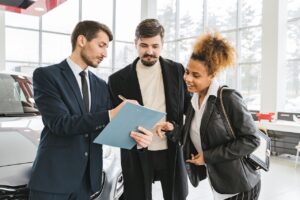car salesman talking with two customers in a dealership showroom
