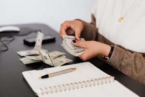 person counting cash at a desk with a pen and notebook