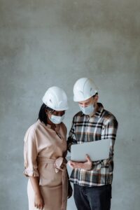 Two people with hardhats and masks looking at a blueprint