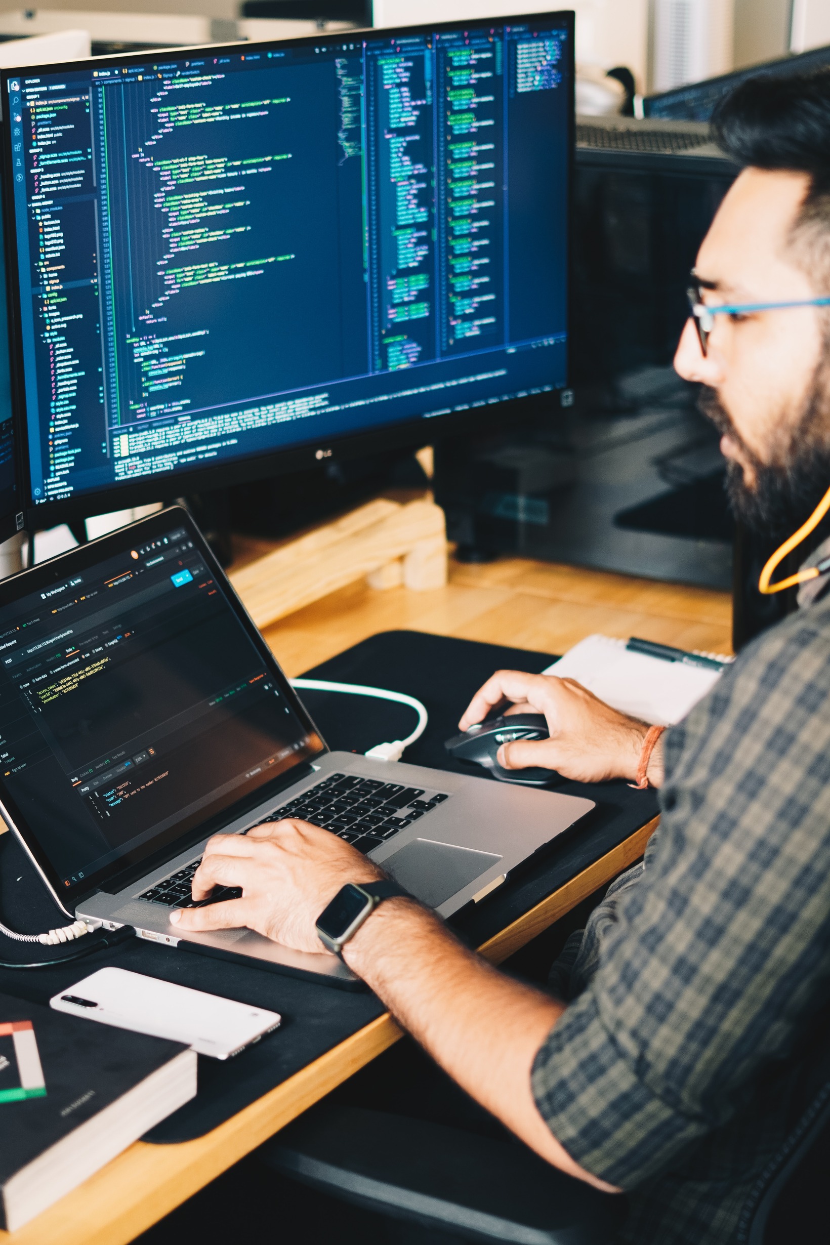 A person working on code on a laptop and a desktop.