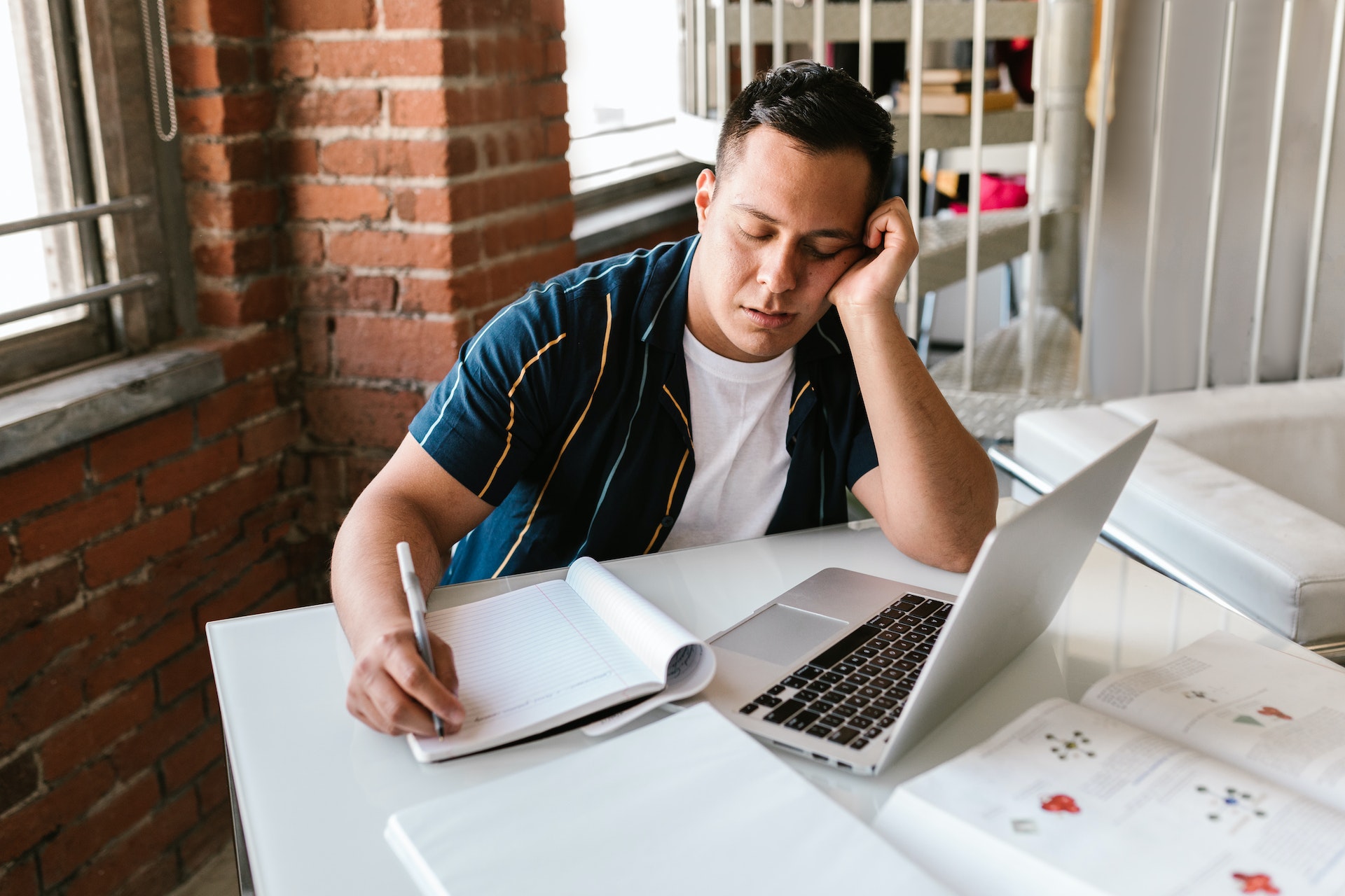 Image of a person dozing off while taking notes on something on their computer.