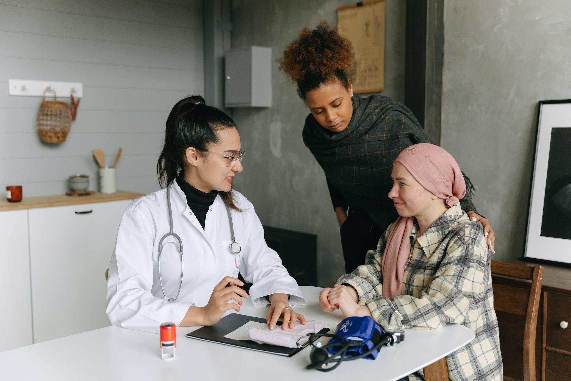 Two women speaking with a doctor who is taking notes, blood pressure cuff on table