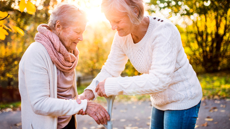 A woman helping an older woman with holding a cane.
