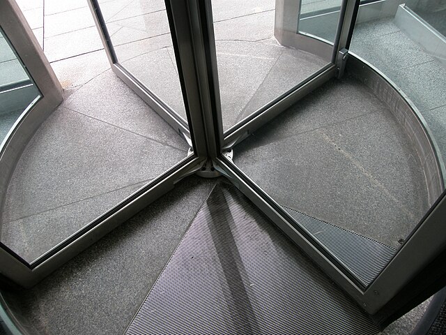 A close-up view of a revolving door. The door is divided into four compartments by metallic frames.