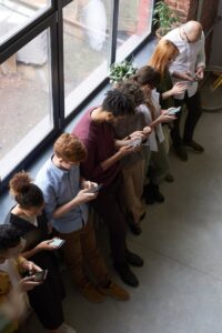 Co-workers standing in a row all looking down at smartphones