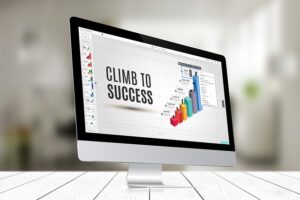 A presentation slide is displayed on a monitor. The slide shows a bar graph and the title, "Climb to Success."