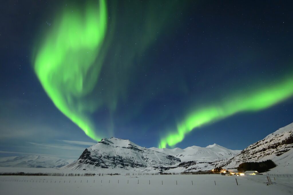 The northern lights forms streaks of green in a dark sky above a snow covered landscape