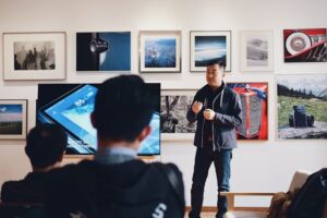 Person standing in front of a wall of framed images giving a speech