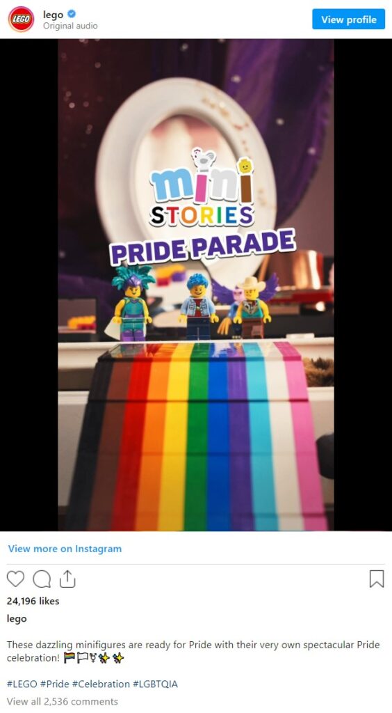 An Instagram post from LEGO's official account features a scene with LEGO minifigures participating in a Pride parade. The background shows a circular white structure with the text "mini STORIES PRIDE PARADE" prominently displayed. Three colorful minifigures are standing on a LEGO-built rainbow pathway that includes brown, black, red, orange, yellow, green, blue, and purple stripes. The caption reads, "These dazzling minifigures are ready for Pride with their very own spectacular Pride celebration! 🏳️🌈🏳️⚧️🎉✨⭐️ #LEGO #Pride #Celebration #LGBTQIA." The post has 24,196 likes and 2,536 comments.